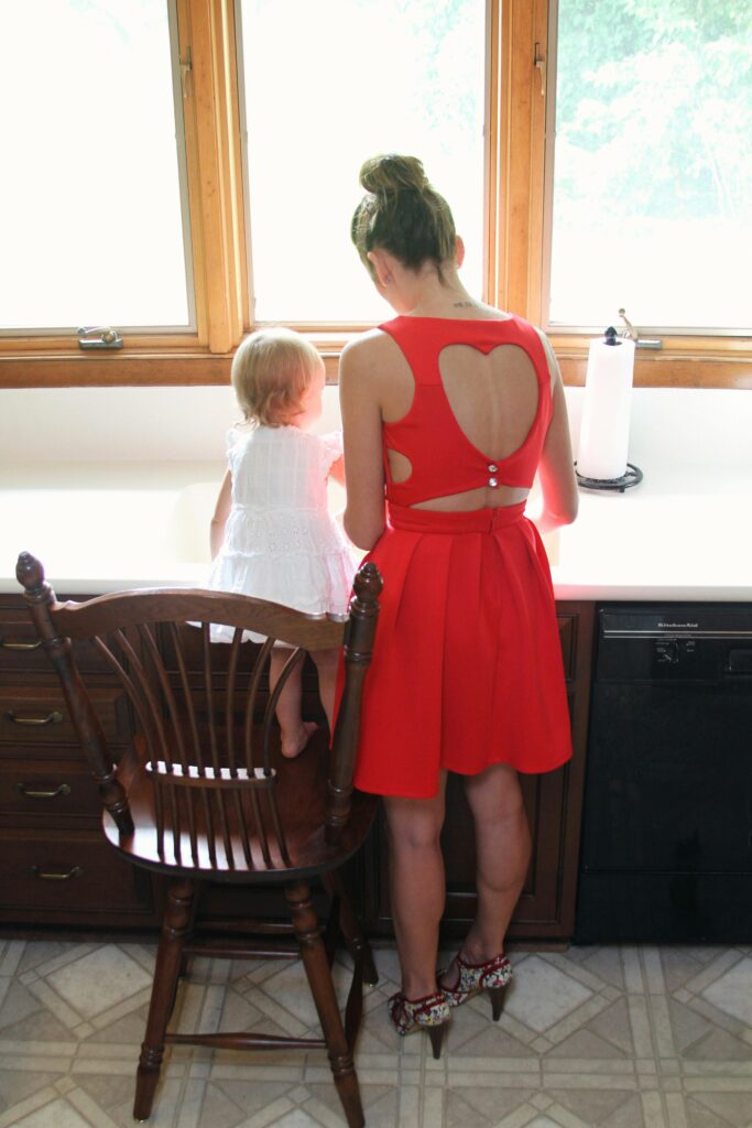 pexels-photo-1089081-1089081 A mother in a red heart dress with her baby on a kitchen chair, looking outside.